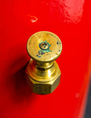 A detailed macro shot captures the functional beauty of a vintage brass control knob set against a vibrant red industrial surface.の素材