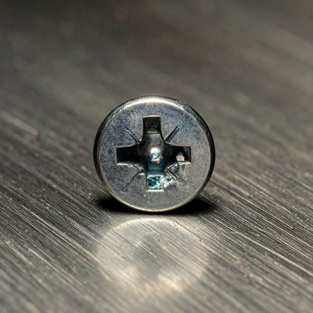 A detailed macro photograph captures the precise engineering of a single Phillips head screw, firmly set into a dark, textured surface.の素材