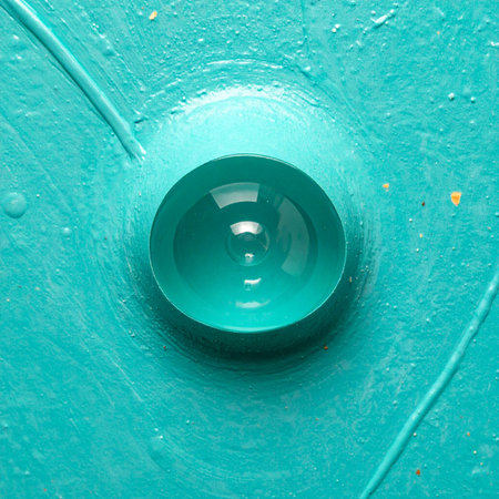 A single, perfect droplet of glossy turquoise paint rests on a textured surface, captured in a stunning macro view.の素材