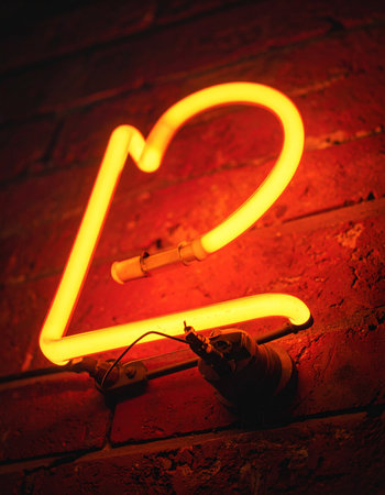 A single neon letter 'P' casts a warm, orange-red glow against a dark brick wall.の素材