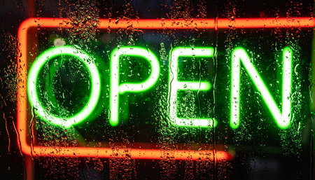 A vibrant green and orange neon 'OPEN' sign glows invitingly through a window covered in raindrops.の素材