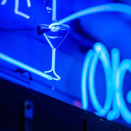 A cool blue neon sign of a martini glass glows intensely in the dark, casting a vibrant reflection.の素材
