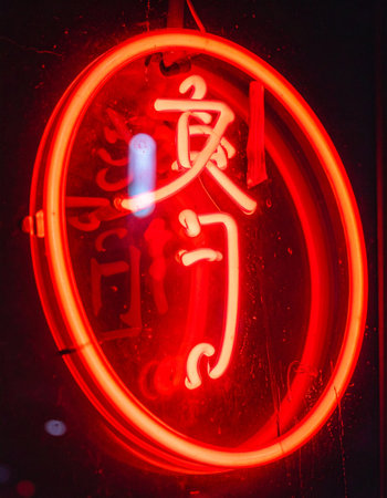 A vibrant red neon sign glows intensely against the darkness, its elegant Chinese calligraphy a beacon in the night.の素材