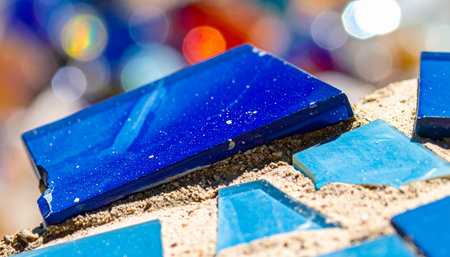 Sunlight catches the deep cobalt and sky blue shards of glass, scattered across a craftsman's workbench.の素材