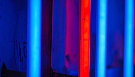 A series of vertical neon tubes cast a vibrant, electric glow. Intense blue light is dramatically interrupted by a single, bold red line, creating a powerful visual contrast.の素材