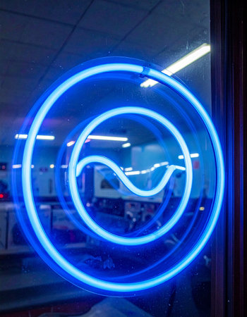 A vibrant blue neon sign glows in a dark window, its concentric circles and central wave creating a futuristic and energetic display.の素材