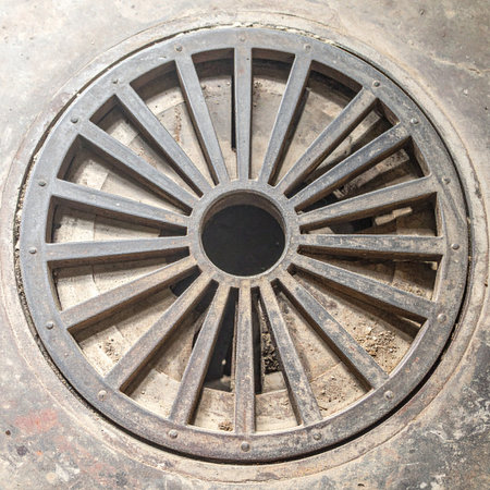 A top-down view captures the robust geometry of a vintage cast iron drain cover, its radial spokes weathered by time and elements.の素材