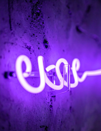A vibrant purple neon sign glows intensely against a dark, textured concrete wall.の素材