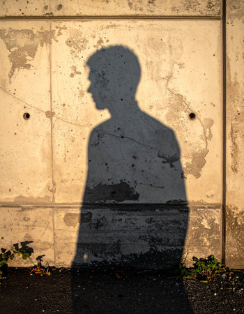 The shadow of a man is cast against a weathered, peeling concrete wall.の素材