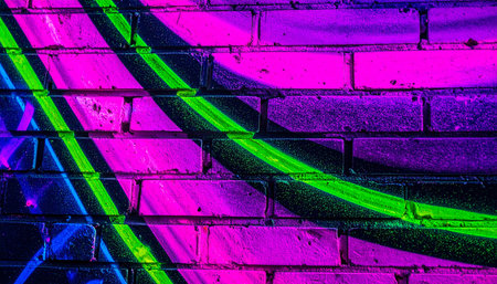 In the heart of the city after dark, a brick wall comes alive with the electric glow of neon graffiti.の素材