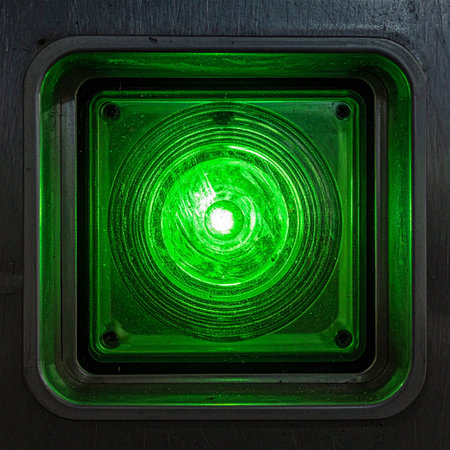 A bright green light glows intensely from a dark industrial panel, signaling that the system is active, online, and ready for operation.の素材