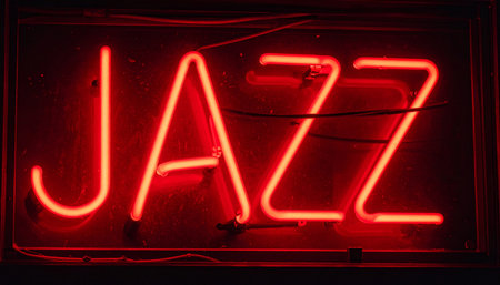 The vibrant red glow of a neon sign cuts through the darkness, spelling out the word 'JAZZ'.の素材