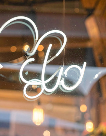A glowing white neon sign, crafted in an elegant cursive script, illuminates a glass window.の素材