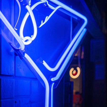 A vibrant blue neon martini glass glows intensely against a dark wall, casting an electric ambiance.の素材