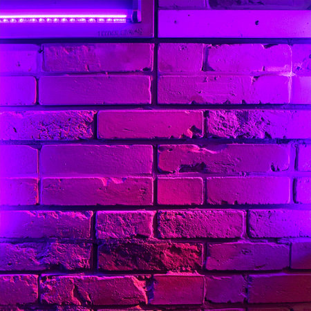 A vibrant purple and pink neon light casts an electric glow across a rugged brick wall, creating a moody and futuristic atmosphere.の素材