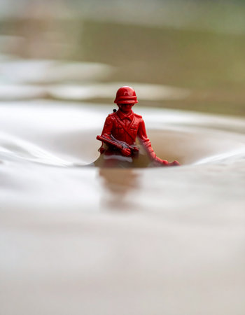 A lone red toy soldier stands firm against the powerful current of a rushing stream.の素材
