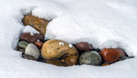A collection of smooth, colorful river stones emerges from a soft blanket of fresh winter snow.の素材
