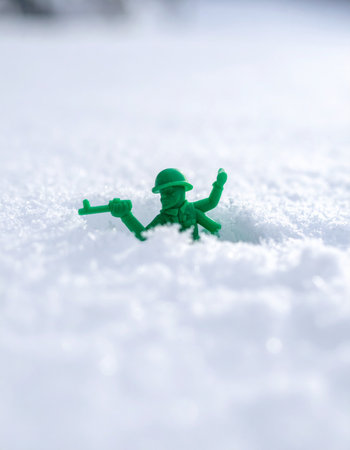 A solitary green toy soldier bravely advances through a vast, unforgiving snowy landscape.の素材