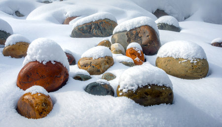 A tranquil winter scene where a fresh blanket of pure white snow gently rests upon a collection of smooth, colorful stones.の素材