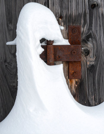 A thick blanket of fresh winter snow clings to a weathered wooden surface, partially obscuring an old, rusty hinge.の素材