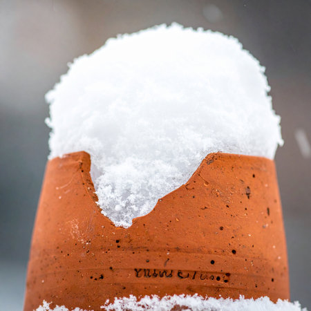 A broken terracotta pot, once a home for summer flowers, now holds a cap of fresh winter snow.の素材