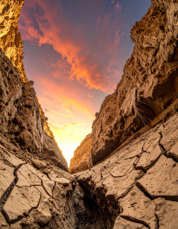 As the sun sets, a fiery sky casts a warm glow over a desolate canyon.の素材
