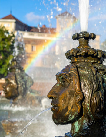 On a brilliant sunny day, a classic bronze fountain comes to life, its spouting water catching the light to create a magical rainbow.の素材