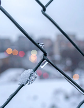 A close-up view of a chain-link fence, where bits of ice cling stubbornly to the cold metal wire.の素材