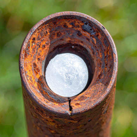 A surprising discovery within a forgotten piece of industry. A bright, moon-like sphere rests inside a heavily corroded and rusted metal pipe, creating a powerful abstract visual.の素材