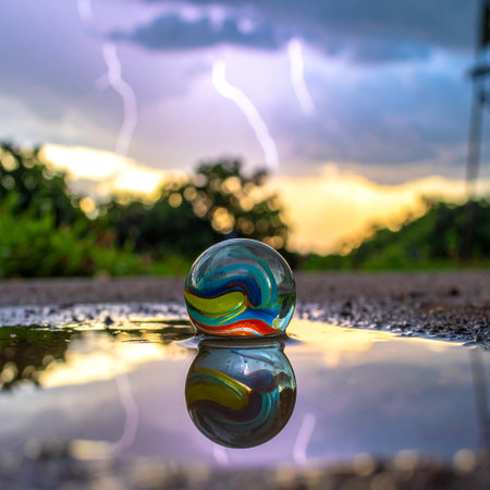 A single glass marble, a world of its own, sits in a shallow puddle after a downpour.の素材