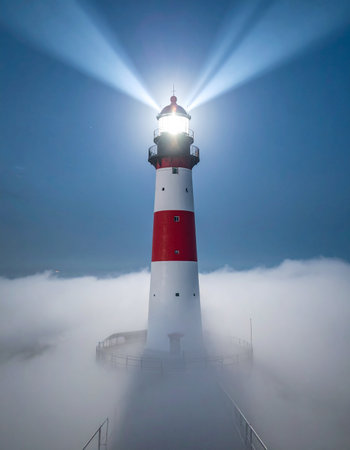 A steadfast lighthouse stands tall, its powerful beacon cutting through a dense blanket of fog.の素材