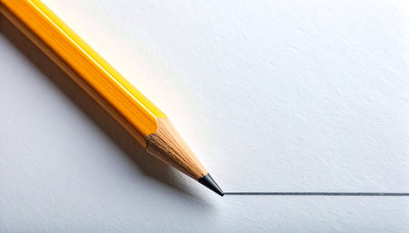 A sharp yellow pencil makes its first mark, drawing a clean, straight line across a blank white page.の素材