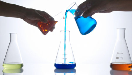 In a brightly lit laboratory, two researchers combine their efforts, carefully pouring colorful chemical solutions into a central flask.の素材