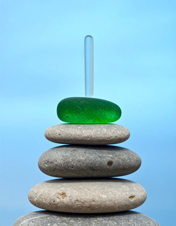 A carefully constructed tower of smooth beach pebbles and weathered sea glass stands in perfect equilibrium.の素材