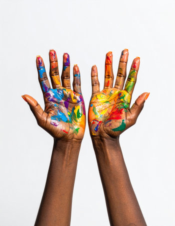 A person's hands covered in a vibrant explosion of paint, held up against a clean white background.の素材