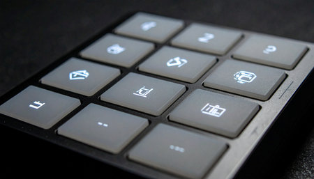 A close-up, angled view of a modern programmable keypad with illuminated icons glowing in a dark setting.の素材