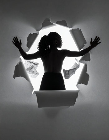 In a dramatic black and white scene, the silhouette of a powerful woman emerges through a torn paper wall.の素材