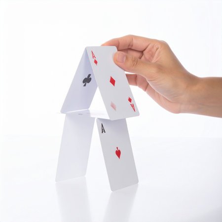 With steady precision, a hand carefully places the final card on a delicate house of cards.の素材