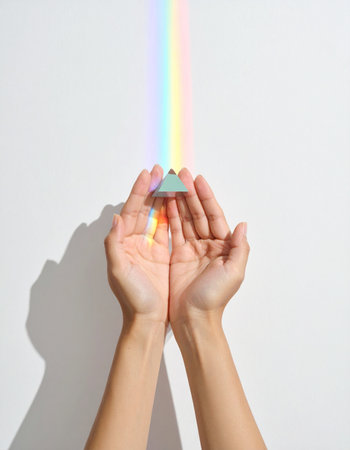 A pair of cupped hands gently holds a small glass prism, transforming a simple beam of light into a vibrant rainbow spectrum.の素材
