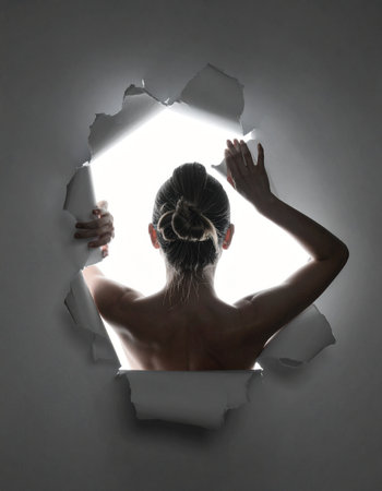 A woman's silhouette is framed from behind as she peers through a torn hole in a dark wall.の素材