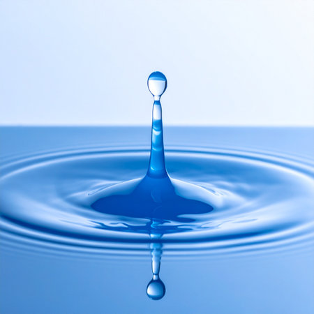 A single, crystal-clear drop of water makes a perfect impact on a calm blue surface, creating a beautiful crown-shaped splash and sending concentric ripples outward.の素材