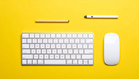 A clean and modern workspace is laid out on a vibrant yellow background, featuring a sleek wireless keyboard, mouse, and digital styluses.の素材