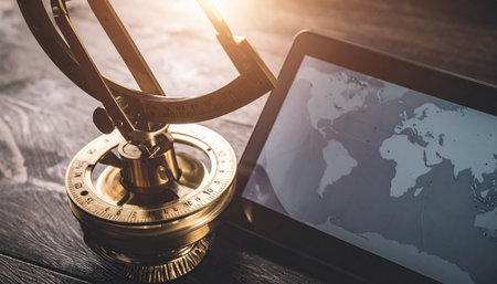 A vintage armillary sphere, a tool of ancient astronomers, sits beside a modern digital tablet displaying a world map.の素材
