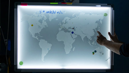 In a dimly lit command center, a strategist's hand points to a key location on a glowing interactive world map, analyzing global data to make a critical business decision.の素材