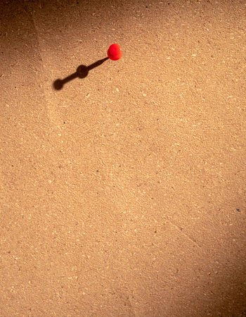 A single red pushpin casts a long, dramatic shadow across a textured corkboard, highlighting a specific point of focus.の素材