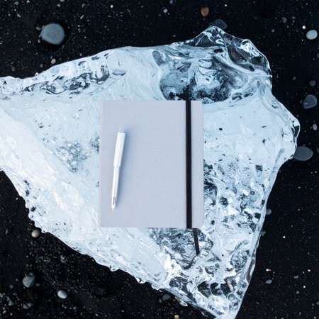 In this conceptual still life, a blank notebook awaits inspiration, placed upon a textured ice formation.の素材