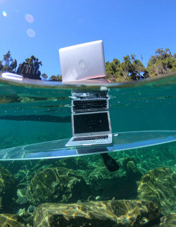 A laptop rests on a transparent surfboard, perfectly balanced between the sunny sky and the clear underwater world.の素材
