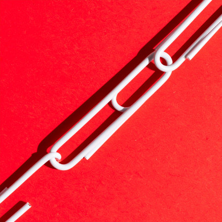 A minimalist, high-contrast image of a white paperclip chain set against a vibrant red background.の素材