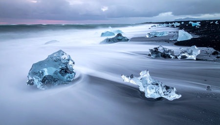 At the edge of Iceland, the ethereal light of dawn kisses ancient glacial ice resting on a volcanic black sand beach.の素材