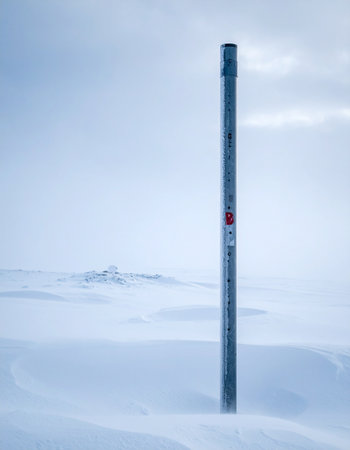 In the heart of a frozen wilderness, a single pole pierces the endless white of a snow-covered landscape.の素材